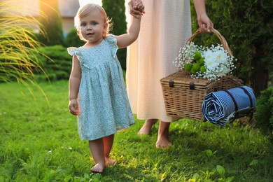 Photo of Adorable baby girl and her mother with picnic basket in garden on sunny day