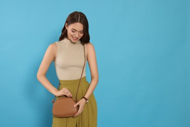 Photo of Beautiful young woman in fashionable outfit with stylish bag on light blue background, space for text