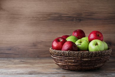 Photo of Fresh ripe green and red apples with water drops in wicker bowl on wooden table, space for text