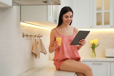 Photo of Young woman with tablet having breakfast in kitchen. Morning routine