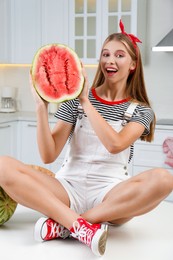 Beautiful teenage girl with half of watermelon on table in kitchen