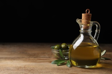 Glass jug of oil, ripe olives and green leaves on wooden table. Space for text