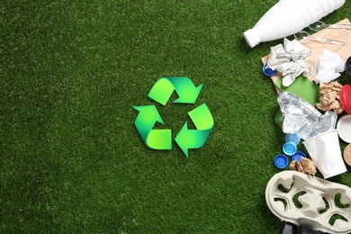 Flat lay composition with recycling symbol, different garbage and space for text on green grass