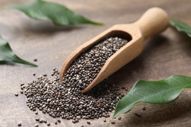 Photo of Scoop with chia seeds and fresh leaves on wooden table
