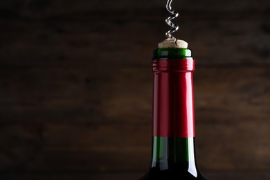 Photo of Opening wine bottle with corkscrew on dark brown background, closeup. Space for text