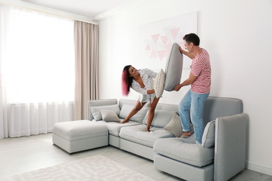 Happy couple having pillow fight on sofa at home