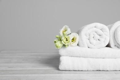 Soft white towels with flowers on wooden table against grey background, space for text