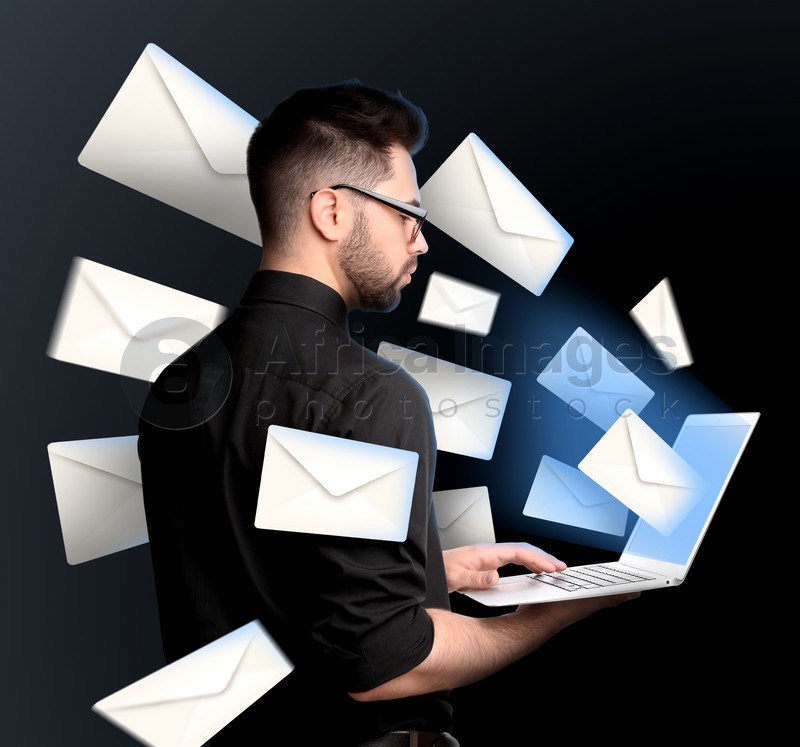 Image of Email spam. Young man with laptop and many letters on black background