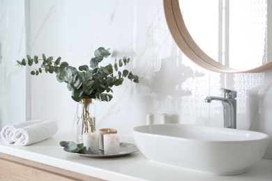Photo of Fresh eucalyptus branches and burning candles on countertop in bathroom