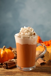 Photo of Delicious pumpkin latte and cinnamon on wooden table, closeup