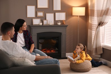 Happy family reading book together near fireplace at home