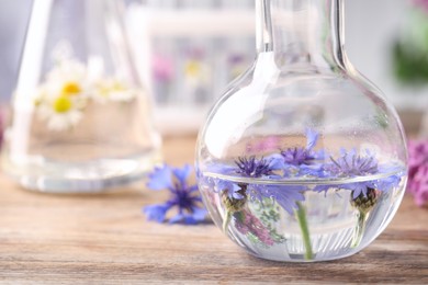 Flask with cornflowers on wooden table, closeup. Essential oil extraction