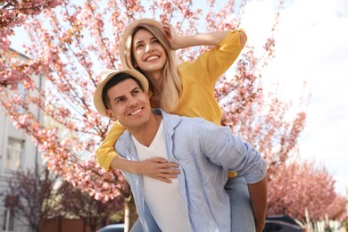 Happy stylish couple near blossoming sakura tree on city street. Spring family look