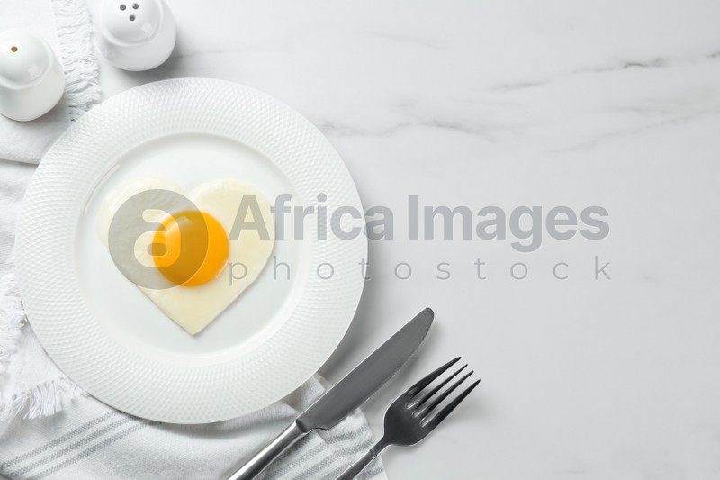 Heart shaped fried egg served on white marble table, flat lay. Space for text