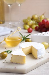 Tasty brie cheese with olives and rosemary on white board