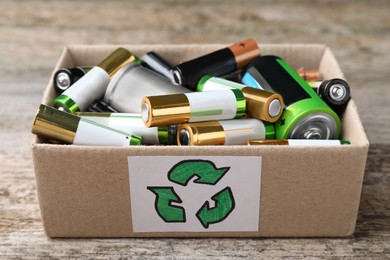 Image of Used batteries in cardboard box with recycling symbol on wooden table, closeup