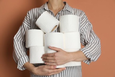 Woman with heap of toilet paper rolls on brown background, closeup