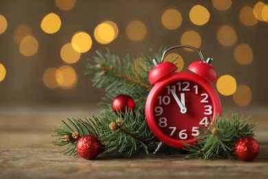 Alarm clock with decor on wooden table against blurred Christmas lights, closeup. New Year countdown