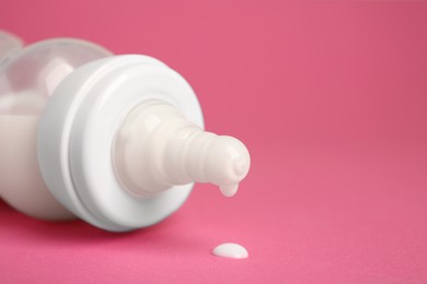 Photo of Feeding bottle with milk on pink background, closeup. Space for text