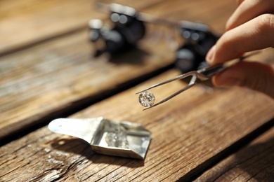 Male jeweler evaluating precious gemstone at table in workshop, closeup