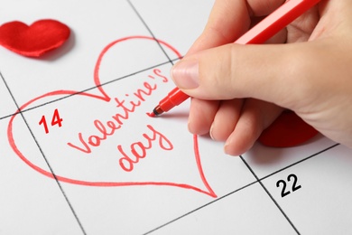 Woman marking Valentine's day with red marker on calendar sheet, closeup