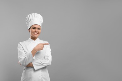 Photo of Happy female chef pointing at something on light grey background. Space for text