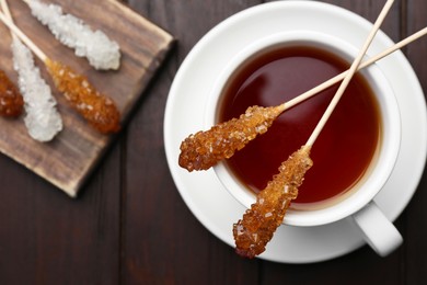 Sticks with sugar crystals served to tea on wooden table, flat lay