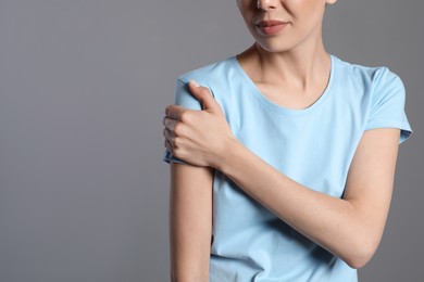 Woman suffering from shoulder pain on beige background, closeup. Space for text