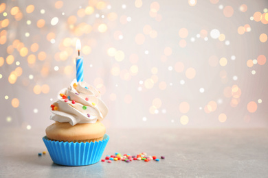 Birthday cupcake with candle on light table, space for text. Bokeh effect