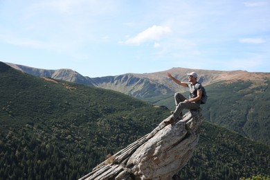 Tourist with backpack enjoying mountain landscape on rocky peak