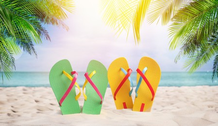Pairs of bright flip flops on sandy beach near sea 