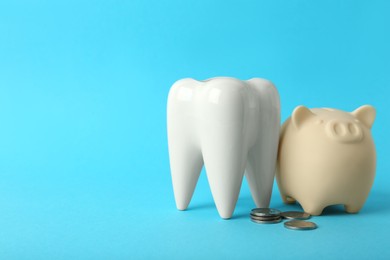 Ceramic model of tooth, piggy bank and coins on light blue background, space for text. Expensive treatment