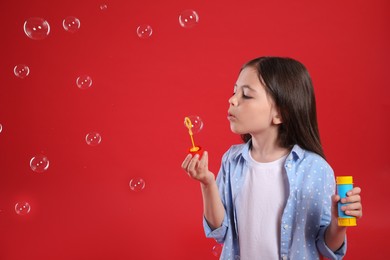 Little girl blowing soap bubbles on red background