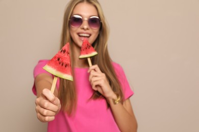 Beautiful girl with pieces of watermelon against beige background, focus on hand