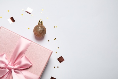 Photo of Pink gift box, Christmas ball and confetti on white background, flat lay. Space for text