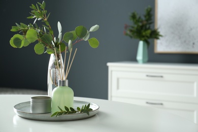 Eucalyptus branches, candle and aromatic reed air freshener on white table indoors, space for text. Interior elements