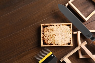 Honeycomb frames and beekeeping tools on wooden table, flat lay. Space for text