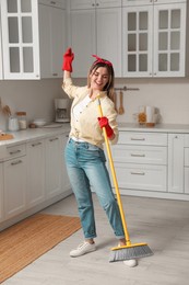 Photo of Woman with broom singing while cleaning in kitchen