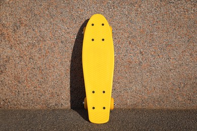 Stylish yellow skate board near wall outdoors