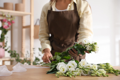 Florist making beautiful bouquet at table in workshop, closeup