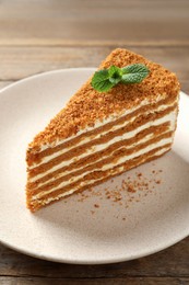 Slice of delicious layered honey cake with mint on wooden table, closeup