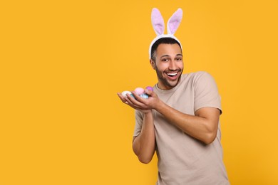 Photo of Happy African American man in bunny ears headband with Easter eggs on orange background, space for text