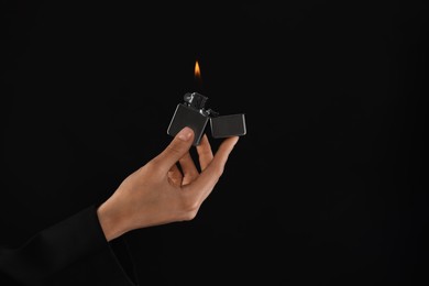 Photo of Woman holding lighter with burning flame on black background, closeup. Space for text