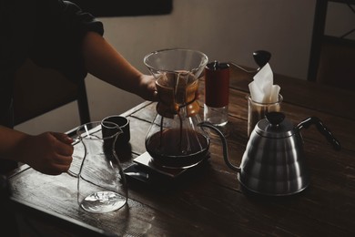 Photo of Barista with coffee maker and jug at wooden table in cafe, closeup
