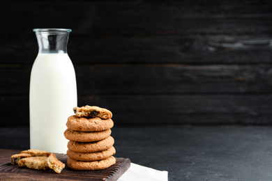 Delicious cookies with raisins and milk on black table. Space for text