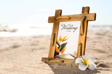 Beautiful wedding invitation and flower on sandy beach, closeup. Space for text