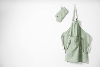 Clean apron with pattern, kitchen tools and oven glove on light wall. Space for text