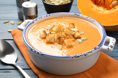 Tasty creamy pumpkin soup with croutons and seeds in bowl on blue wooden table