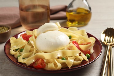 Plate of delicious pasta with burrata, peas and tomatoes on white wooden table, closeup