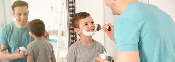 Dad applying shaving foam onto son's face in bathroom. Banner design